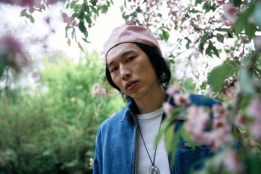 Havalı kot elbiseli Asyalı genç bir adam, canlı çiçeklerle dolu bir parkta dinleniyor..