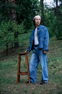 Genç bir adam kendine güvenerek bir parkta duruyor, şık kotlarını ve tavırlarını gösteriyor..