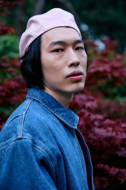 Huzurlu bir parkta, Asyalı genç bir adam son moda bir kostüm giyiyor, zahmetsiz bir stil yayıyor..