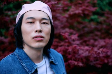 Genç Asyalı bir adam kot pantolonunu renkli bir parkta sergiliyor, kendine güven ve tarz yayıyor..