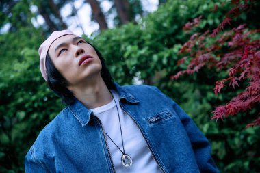 Şık kot elbiseli genç bir Asyalı, yemyeşil bir parkın huzurunun tadını çıkarıyor..