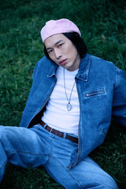 Genç Asyalı bir adam parkta dinleniyor. Pembe şapkalı şık bir kot elbise giyiyor..