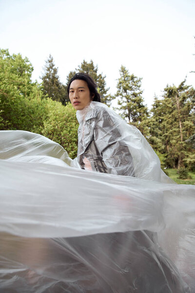 Молодой азиат прогуливается по парку, позируя с полиэтиленом, концепцией устойчивого развития