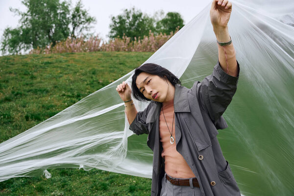 Молодой азиат в сером наряде играет с пластиковым листом в парке.