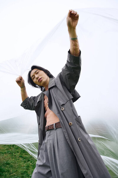 Молодой человек демонстрирует современную моду в сером, наслаждаясь мирным моментом на открытом воздухе, держа полиэтилен