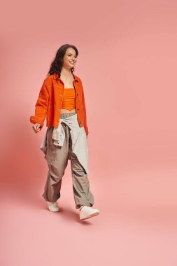 Genç bir kadın zarif bir şekilde yürürken kendine güvenerek modaya uygun kıyafetini gösterir..