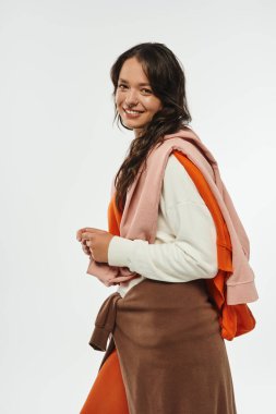 Genç bir kadın modern kapalı mekan aydınlatmasında gülümserken moda kıyafetlerini sunar..