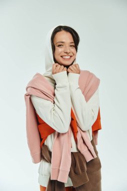 Genç bir kadın neşeyle parıldıyor, modaya uygun giysi katmanlarıyla sarmalanmış..