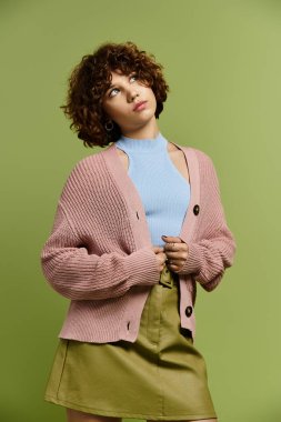 Genç bir kadın yeşil arka planda kendine güvenen şık kıyafetini sergiliyor..