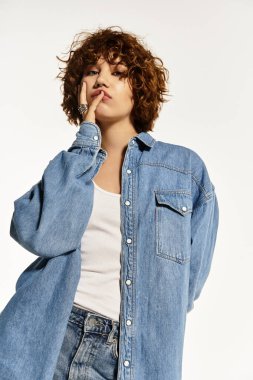 Kendine güvenen genç bir kadın kısa kıvırcık saçlı şık bir kot gömlek ve kot pantolon giyiyor..