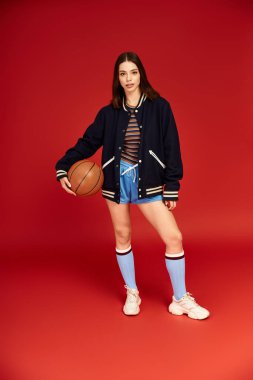Şık giyinmiş genç bir kadın basketbol topuyla kendine güvenir, tarzını ön plana çıkarır..