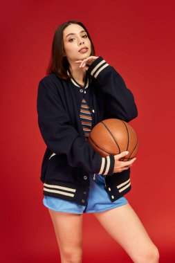 Şık, genç bir kadın basketbol topuyla poz veriyor. Kalın bir zemine karşı şık giyiniyor..