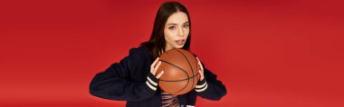 Genç bir kadın, kırmızı bir zemine karşı basketbol topuyla poz verirken kendine güvenini gösteriyor..