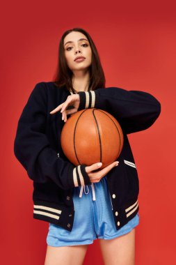 Şık, genç bir kadın canlı bir arka plana karşı basketbol topuyla güven içinde poz veriyor..