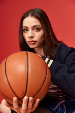 Kendine güvenen bir kadın modern bir ortamda basketbol topunu tutarken şık tarzını sergiliyor..