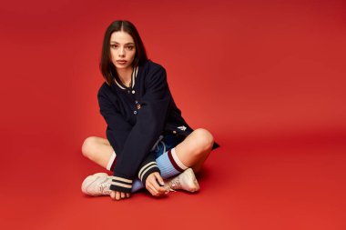 Moda kıyafetli genç bayan yerde rahatça oturuyor, kendine güven ve zarafet saçıyor..