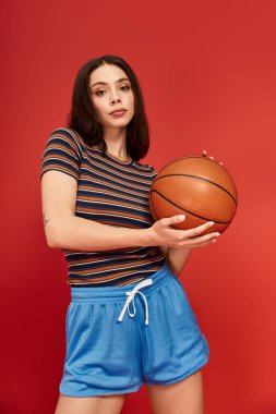 Renkli giyinmiş kendine güvenen bir kadın canlı bir arka plana karşı basketbol topuyla poz veriyor..