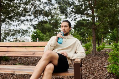 Kendini işine adamış genç bir adam, doğanın sükûnetinin ortasında dışarıda egzersiz yaparken susuzluğunu giderir..