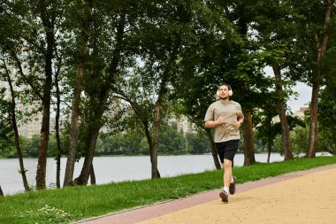 Sakallı genç bir adam nehir boyunca koşuyor, doğa ve uygunluğu kucaklıyor..