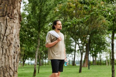 Sakallı genç bir adam sakin bir açık hava ortamında egzersiz yapmaya ara veriyor..