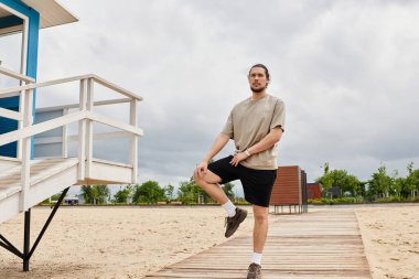 Genç atletik bir adam bir cankurtaran istasyonunun yanındaki kumlu yolda egzersiz yapıyor..