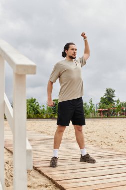 Sakallı genç bir adam dışarıda egzersiz yapıyor, gücünü ve azmini gösteriyor..