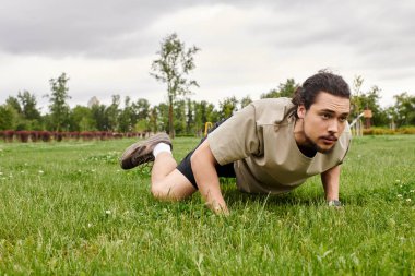 Sportif genç adam bulutlu bir gökyüzünün altında çimenli bir alanda şınav çekiyor, fitness üzerine odaklanıyor..