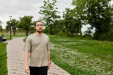 Sakallı genç adam açık havada egzersiz yapmayı seviyor. Canlı bir parkta atletizm sergiliyor..