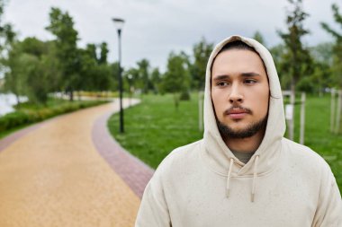 Genç bir adam parkta yürürken rahat bir kapüşonluyla atletizmini sergiliyor..