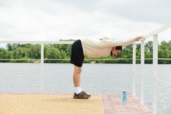 Young man stretches on a dock while preparing for an outdoor workout session by the water.