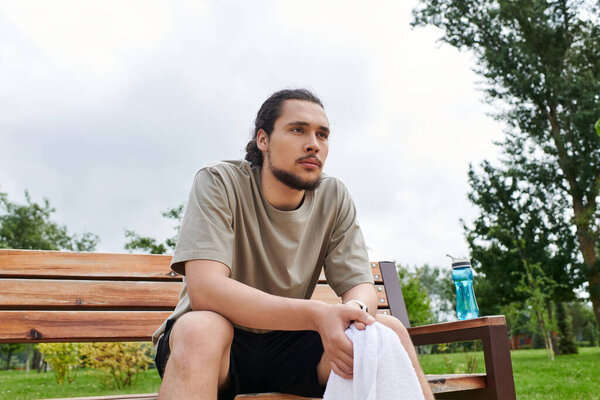 Спортивный молодой человек с бородой покоится на скамейке после бодрящей тренировки на открытом воздухе.