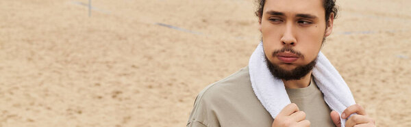 Молодой человек с бородой готовится к тренировке на песчаном пляже, сосредоточенный и решительный, баннер