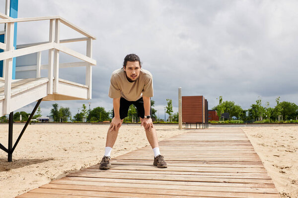 Молодой спортсмен делает паузу, чтобы отдышаться, занимаясь спортом на открытом воздухе возле пляжа..
