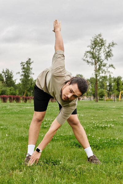 Young athletic man performs a deep stretch in a lush green park surrounded by nature.