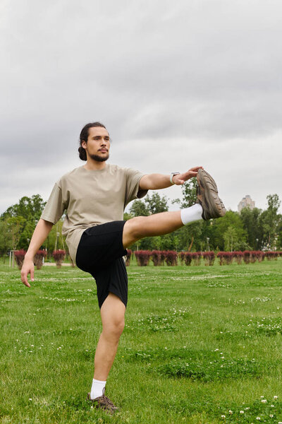 Sporty young man stretches while exercising on grassy field under a cloudy sky.