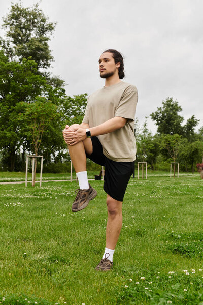 A bearded man stretches his legs in a lush outdoor setting, boosting his fitness.