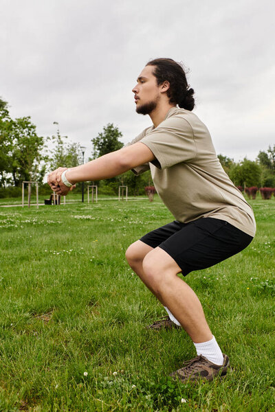 Молодой человек интенсивно тренируется, делая приседания в открытом парке, окруженный природой.