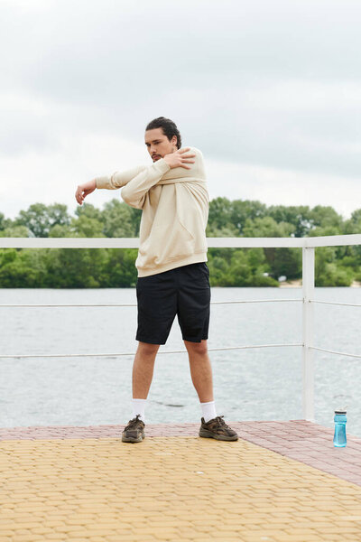 Молодой человек в толстовке выступает на открытом воздухе у живописной набережной.