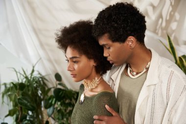 Bir çift, bitkilerle dolu şık, bereketli bir salonda sevgiyle kucaklaşır..