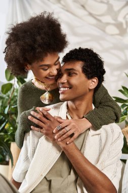 Sevgi dolu bir çift, şık bir iç mekandaki yemyeşil bitkilerle nazikçe kucaklaşır..