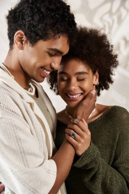 İki genç aşık neşeli bir şekilde kucaklaşıyor, derin bağlantılarını moda bir ortamda sergiliyorlar.