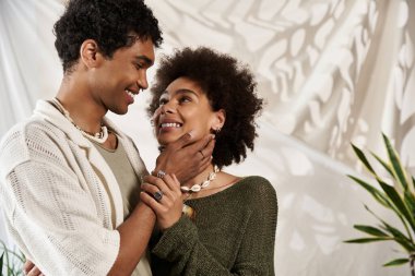 Sevgi dolu genç çiftler, parlak ve rahat bir ortamda kucaklaşırken birbirlerinin gözlerine bakarlar.