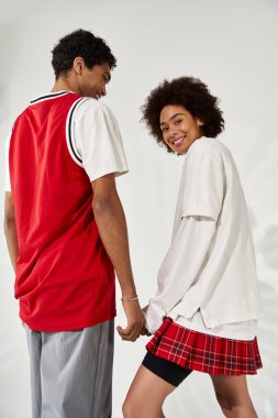 Neşeli genç çift, modaya uygun günlük kıyafetler giyerken hafif bir arka plana karşı sevgi gösteriyor..