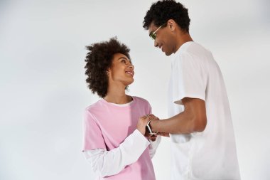 Bir çift birbirine yakın duruyor, gülümsüyor, elleri şık bir stüdyo ortamında sıkıca bağlı..