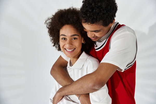 In a cozy setting, a young couple embraces, smiling and showcasing their stylish looks.