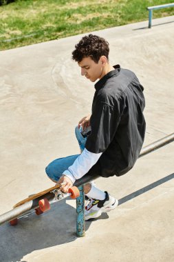 Genç bir adam elinde kaykayıyla korkulukta dengede duruyor, güneşli bir günün tadını çıkarıyor..