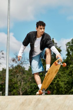 Genç bir adam parlak bir gökyüzünün altındaki manzaralı parkta şık bir kaykay numarası yapıyor..