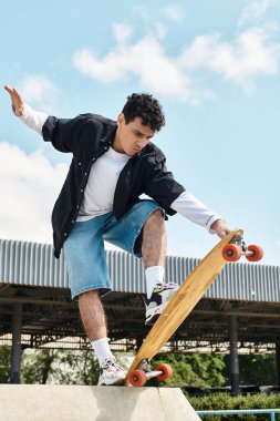 Genç bir adam dışarıda güzel bir günün tadını çıkarırken parkta kaykayıyla oyun oynuyor..