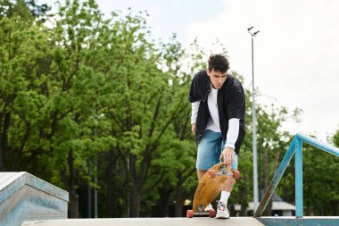 Genç bir adam kaykayını ustalıkla yeşil ve güneşli bir parkta sürüyor..