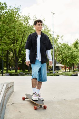 Genç bir adam kaykayını yeşil ve güneşli bir parkta sürüyor..